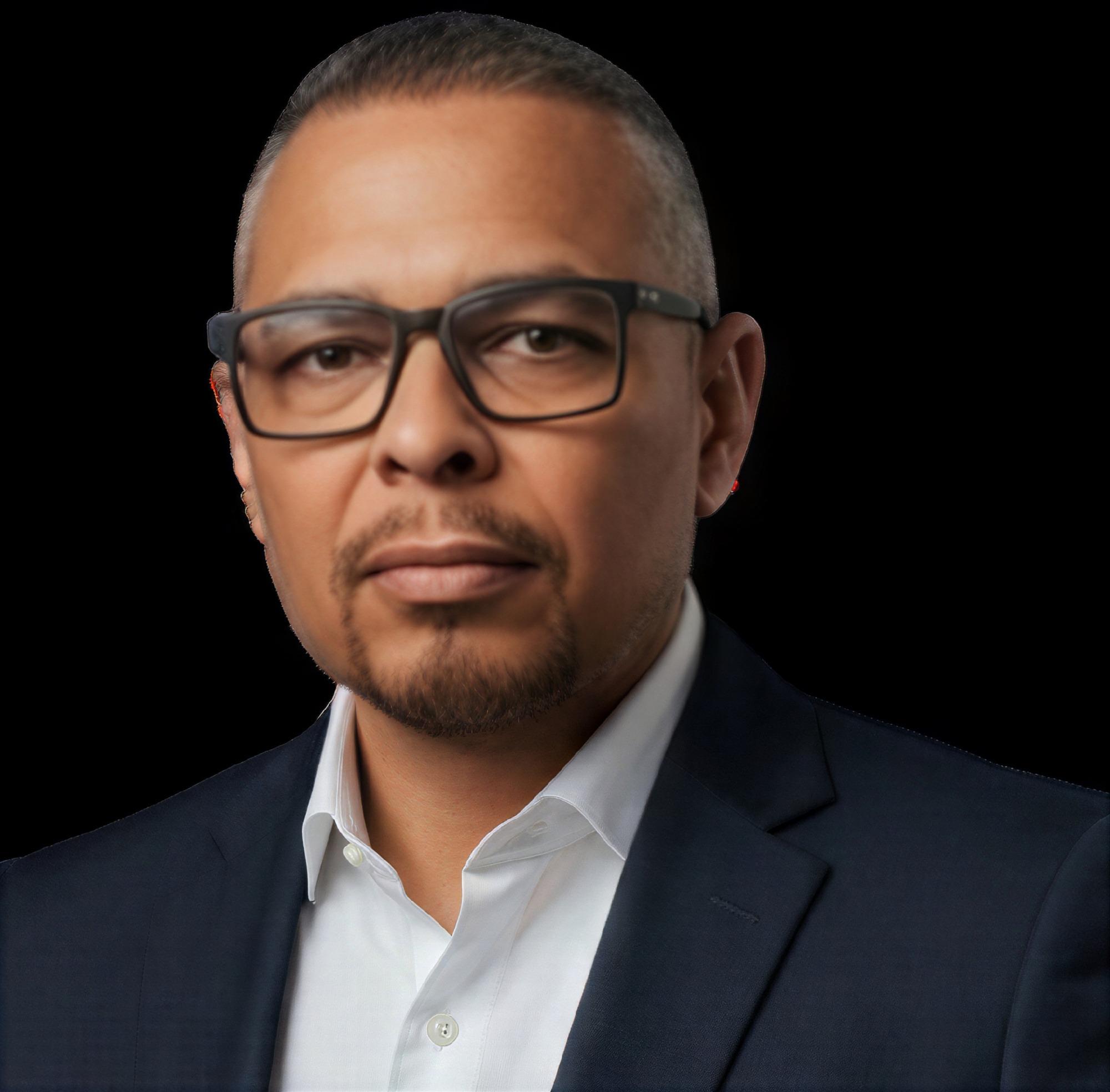 Christopher Thompkins wearing glasses, a dark suit jacket, and a white shirt.